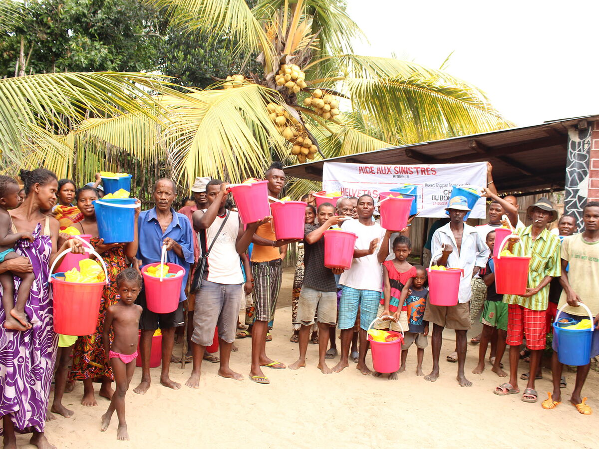 Many families with children are standing with buckets in front of a house.