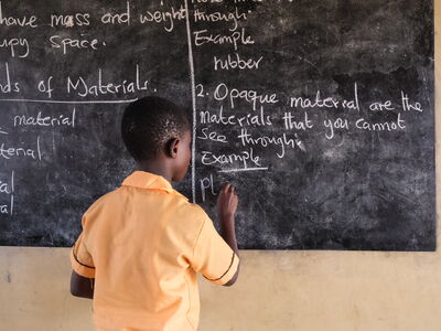 A pupil writes with white chalk on a blackboard.