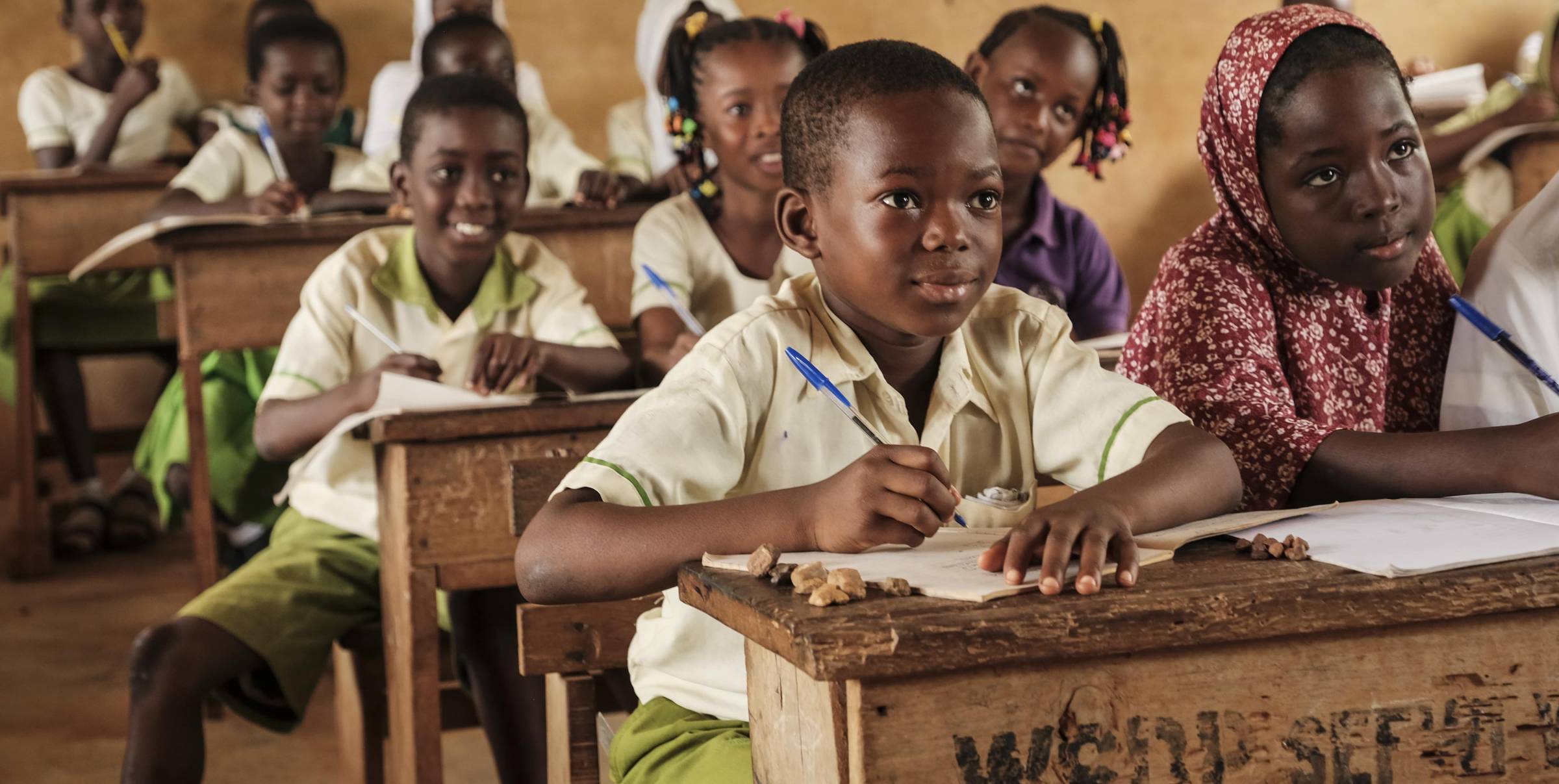 Many children with a pen in hand and a notebook on old wooden tables.